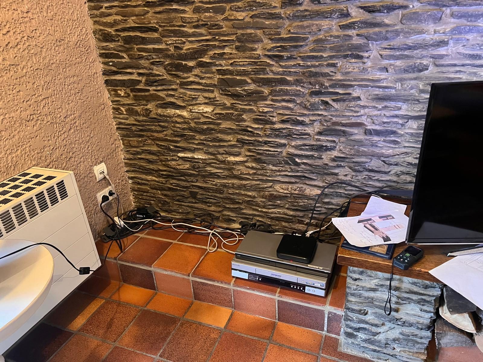 Maison privée — le coin télé avant travaux, câbles apparents sur le mur en pierre